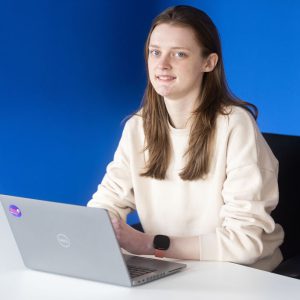 Young female engineer with brown hair and a white jumper sat typing on a laptop.